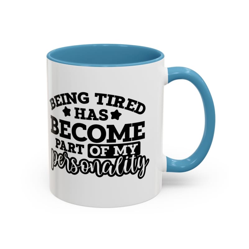 White coffee mug with blue handle and interior featuring black text that reads ’Being tired has become part of my personality’