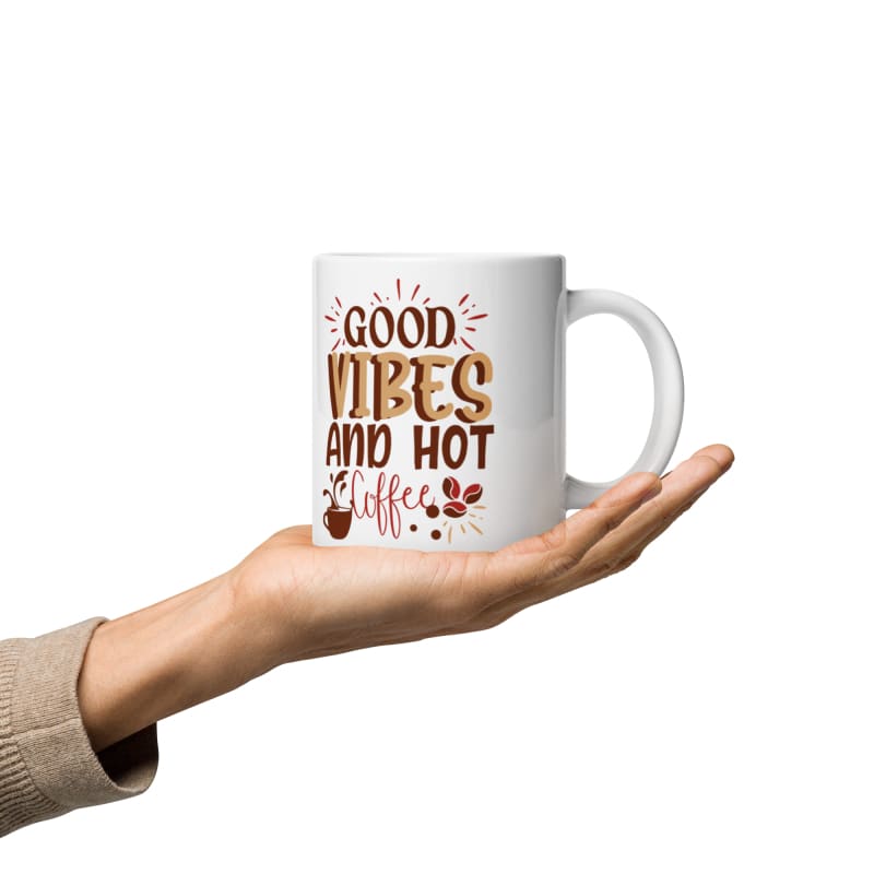 White mug with ’Good Vibes and Hot Coffee’ text held by a hand.