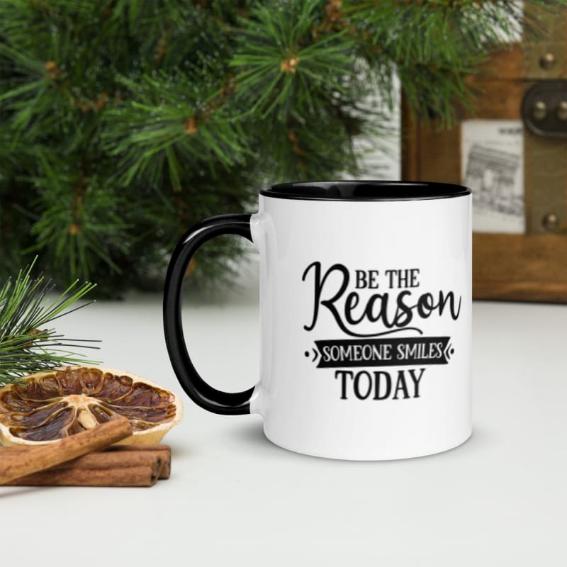 White mug with black handle and inspirational text saying ’Be the Reason Someone Smiles Today’.