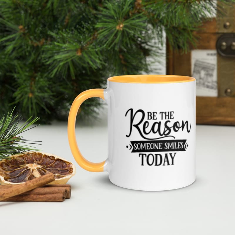 White mug with yellow interior and handle, featuring the motivational text ’Be the Reason Someone Smiles Today’.