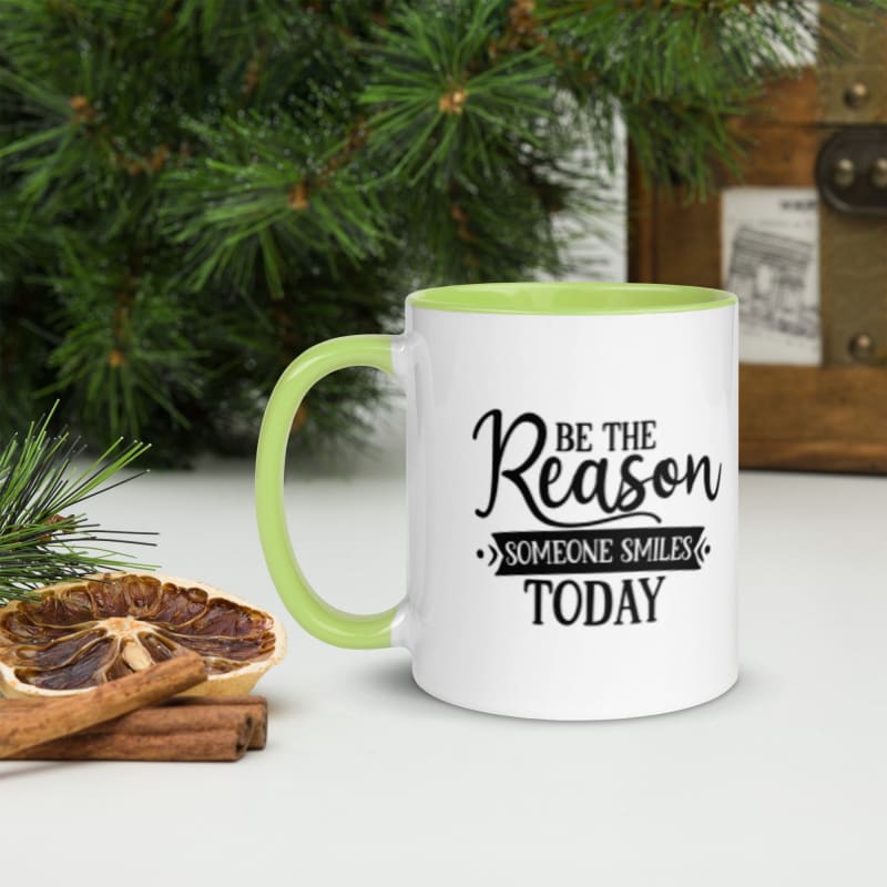 White mug with green handle and rim featuring the text ’Be the Reason Someone Smiles Today’.