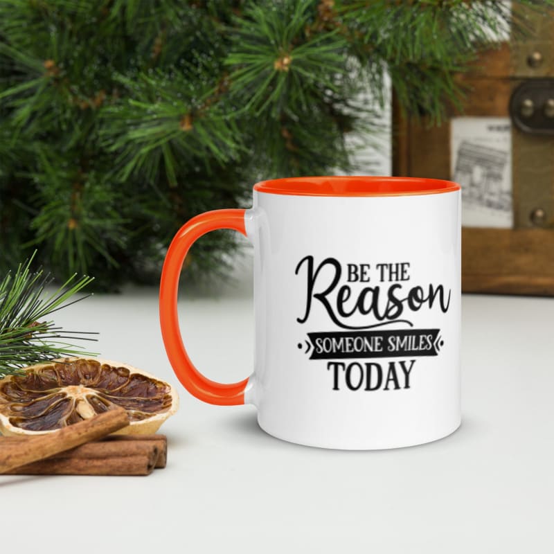 White mug with orange handle and rim featuring the motivational text ’Be the Reason Someone Smiles Today’.