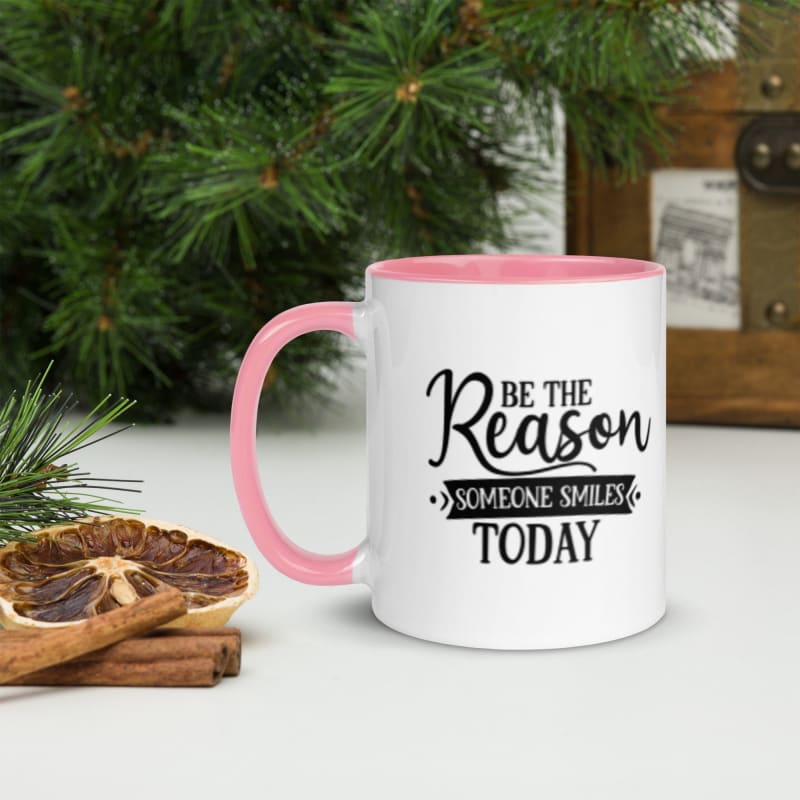 White mug with pink handle and rim featuring the text ’Be the Reason Someone Smiles Today’.