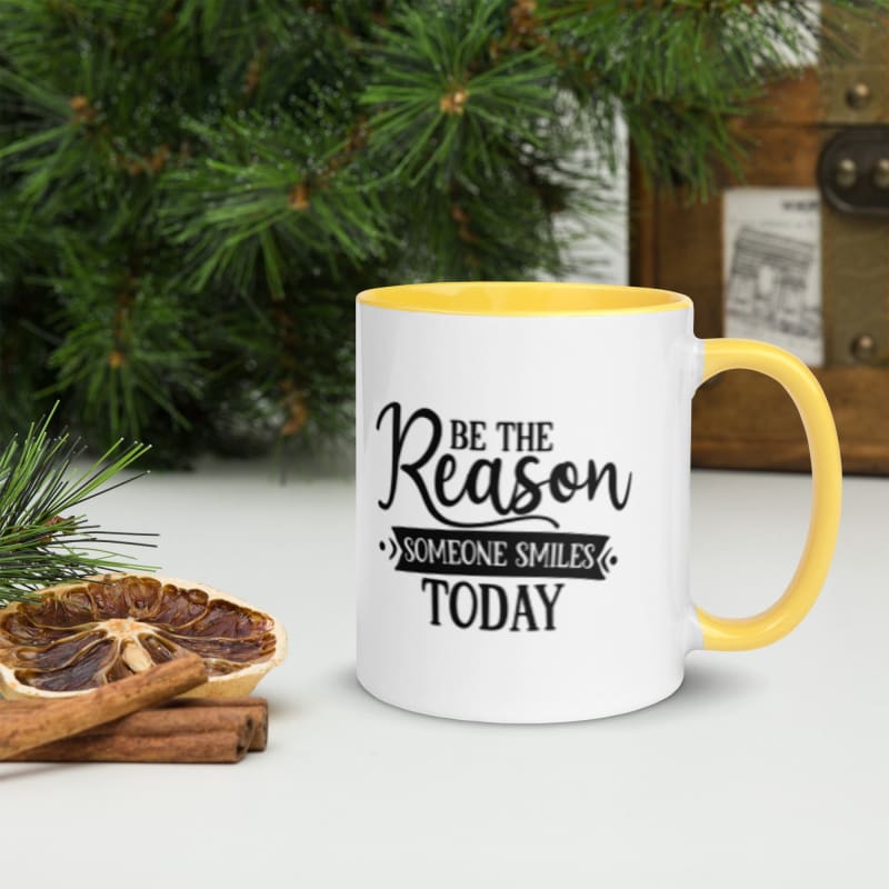 White mug with yellow handle and inspirational text saying ’Be the Reason Someone Smiles Today’.