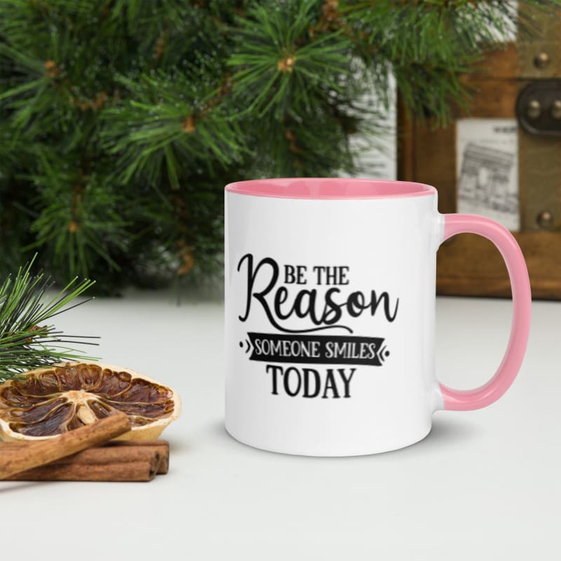 White coffee mug with pink handle and inspirational text saying ’Be the Reason Someone Smiles Today’.