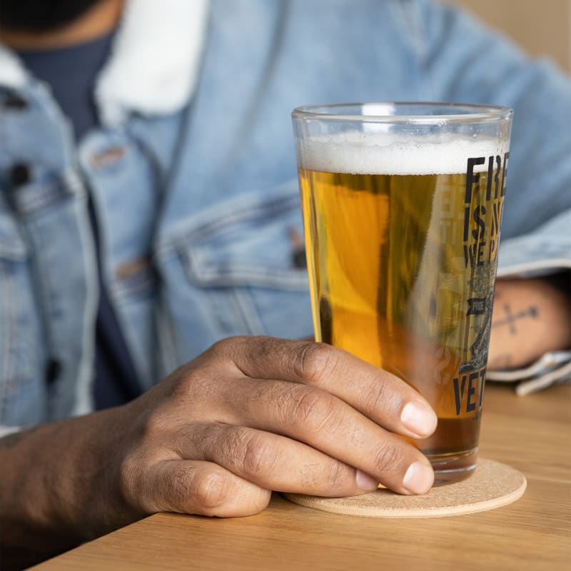 Glass of beer held by a hand on a wooden surface.