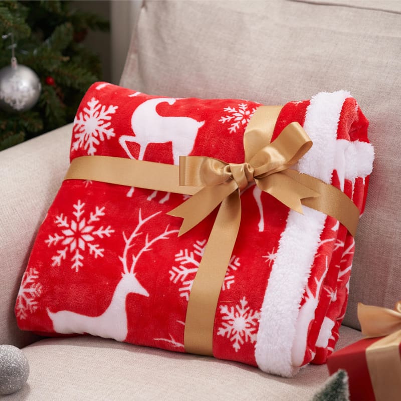 Red and white holiday blanket with reindeer and snowflake patterns tied with a gold bow.