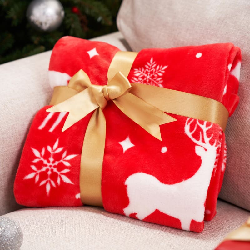 Red fleece blanket with white reindeer and snowflake pattern tied with a gold bow.