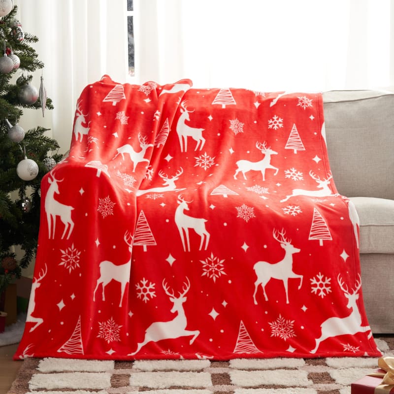 Red fleece blanket with white reindeer, snowflake, and Christmas tree pattern.