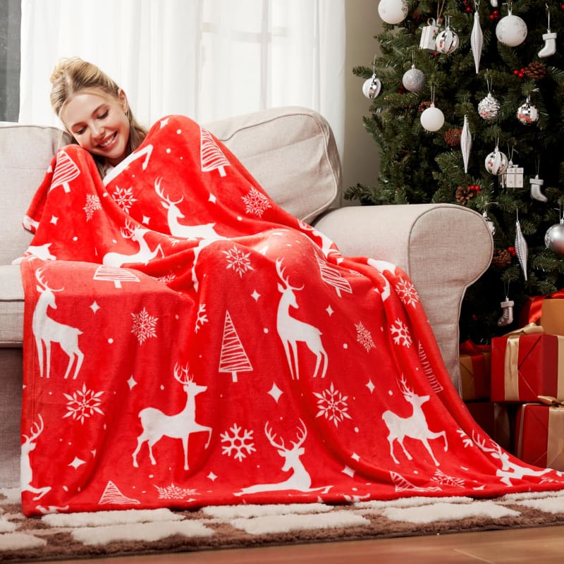 Red fleece blanket with white reindeer and Christmas tree patterns.