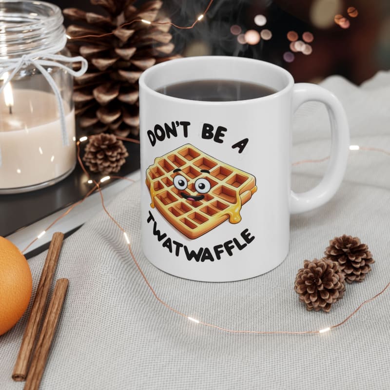 White coffee mug featuring a cartoon waffle design and text that reads ’DON’T BE A TWATWAFFLE’